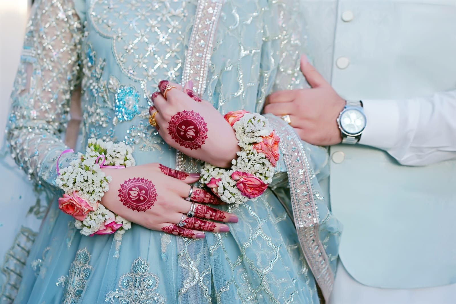 Wedding couple's hands with floral jewelry and embroidered outfits